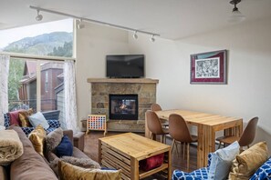 A cozy living room with a fireplace, a television mounted above it, and a dining area with wooden furniture.