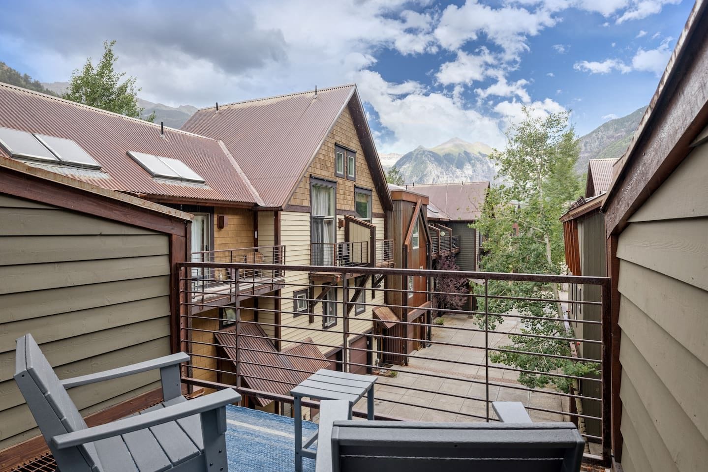 A residential building with multiple levels, a balcony with a metal railing, and a view of mountains in the background.