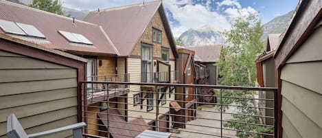 A residential building with multiple levels, a balcony with a metal railing, and a view of mountains in the background.