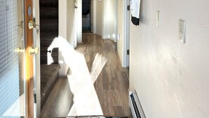 A hallway with a wooden floor, a staircase, a chandelier, and a coat rack.