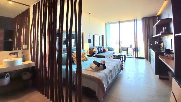 Ein modernes Hotelzimmer mit einem großen Bett, einer Couch, einem Essbereich und Blick ins Freie.