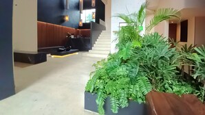 Eine Lobby mit Empfangstresen, einer Treppe und einem großen Pflanzenbeet mit verschiedenen Pflanzen.