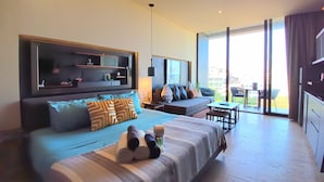 Ein modernes Hotelzimmer mit einem großen Bett, einem Fernseher, einer Couch, einem Esstisch und einem Balkon mit Blick.