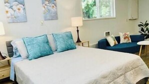 Ein Schlafzimmer mit einem Bett, einem Nachttisch, einer Lampe, einem blauen Sofa und zwei an der Wand befestigten Bildern.