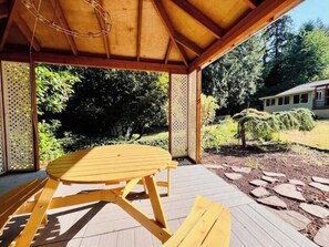 A wooden gazebo with a table and benches, surrounded by a garden with trees and a house in the background. - Cozy 1BR w/ Garden Oasis and Free Parking (Bothell)