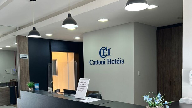 Mostrador de recepción de hotel con un letrero que dice "Cattoni Hotéis" y un aviso indicando a los huéspedes que deben registrar su salida en el mostrador.