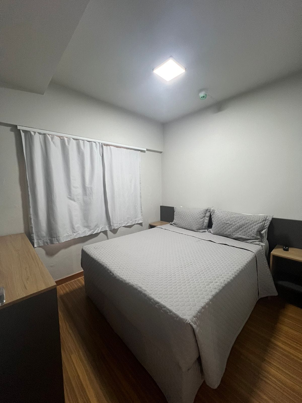 A bedroom with a bed, a nightstand, a wooden dresser, and a window with curtains.