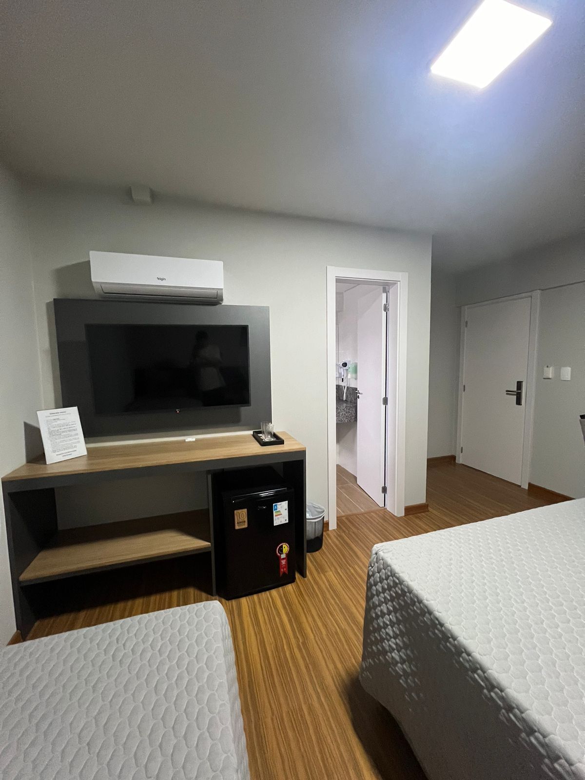 Une chambre d’hôtel équipée d’une télévision, d’un bureau, d’un réfrigérateur, de deux lits et d’une salle de bain visible à travers une porte ouverte.