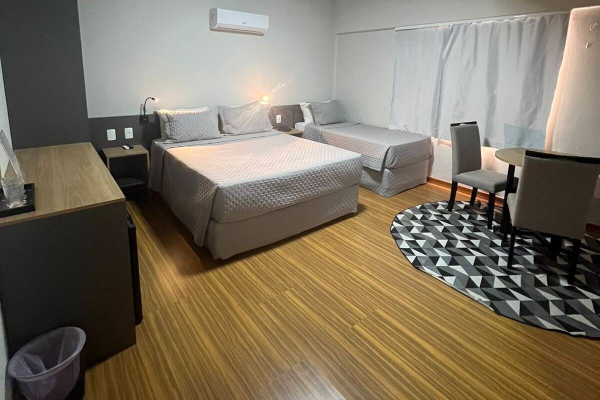 A modern hotel room with a wooden floor, a bed, a desk, a chair, and a small table.