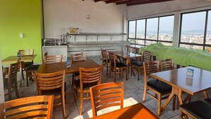 Un restaurante con mesas y sillas de madera, una zona de cocina y ventanas amplias con vistas a la ciudad.