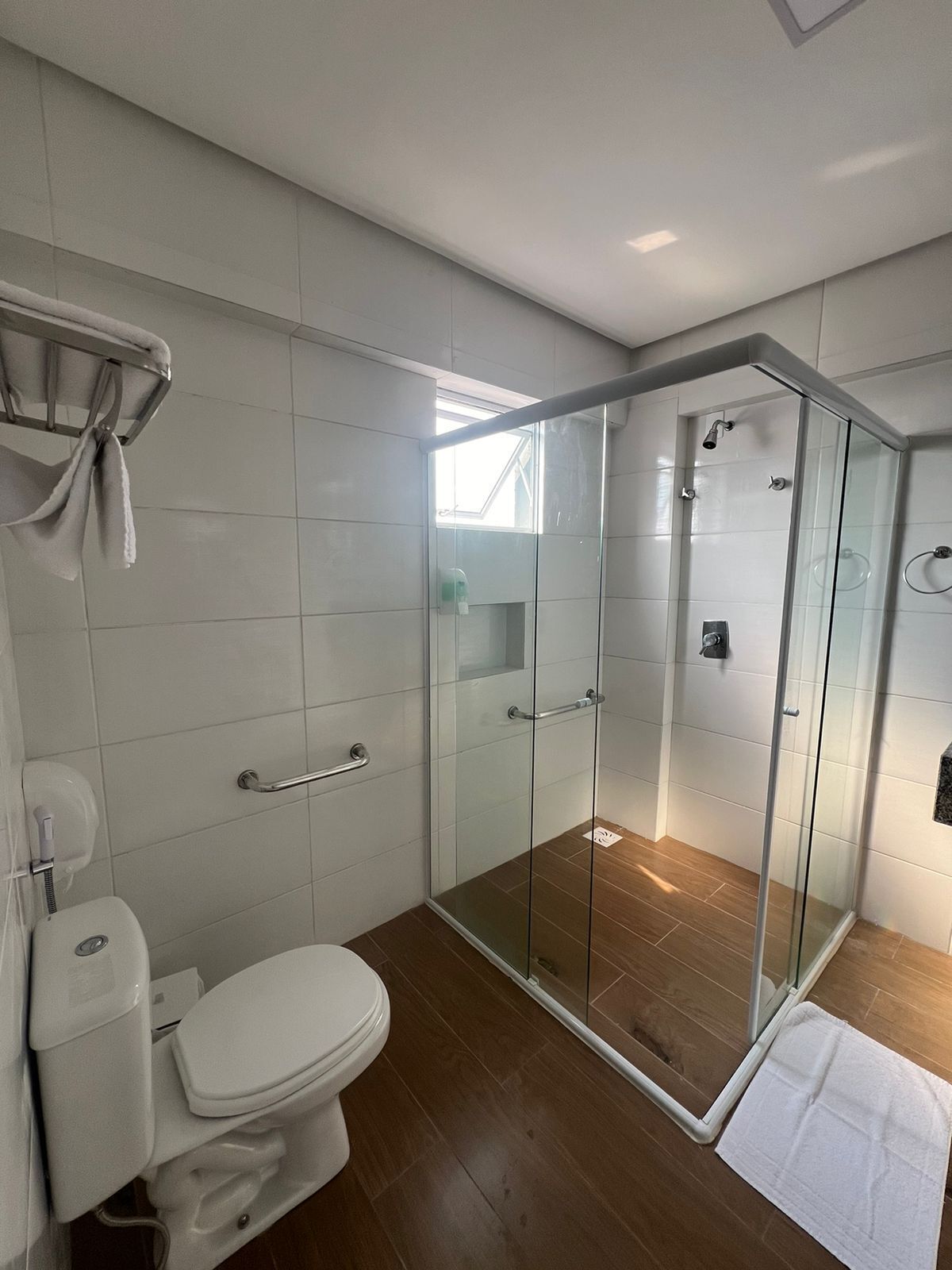 Un baño moderno con ducha envuelta en vidrio, inodoro y toallero.