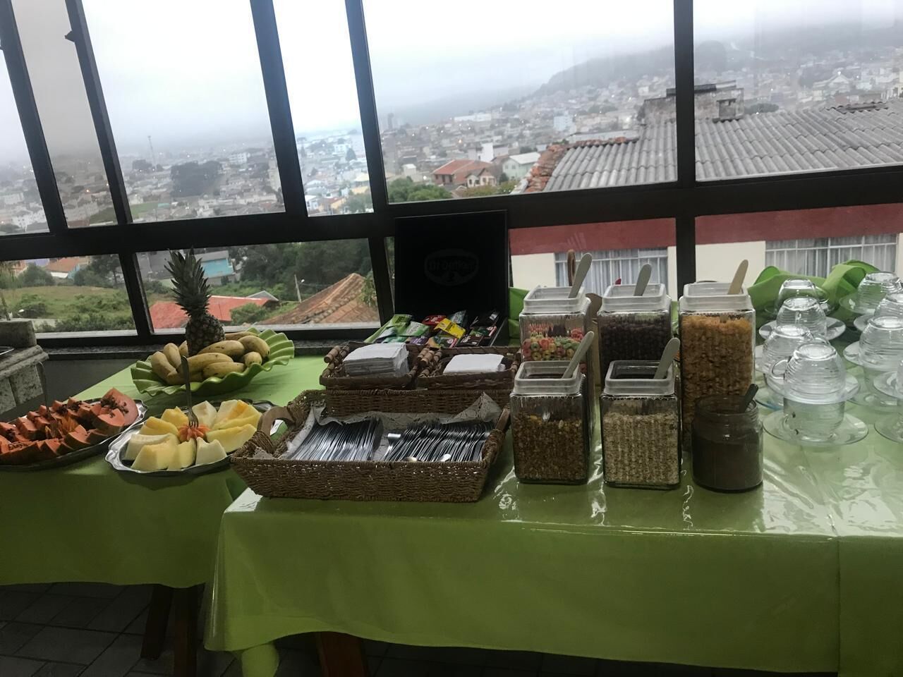 Buffet amb diverses platelles i utensilis, amb una vista de la ciutat a través de grans finestres al fons.