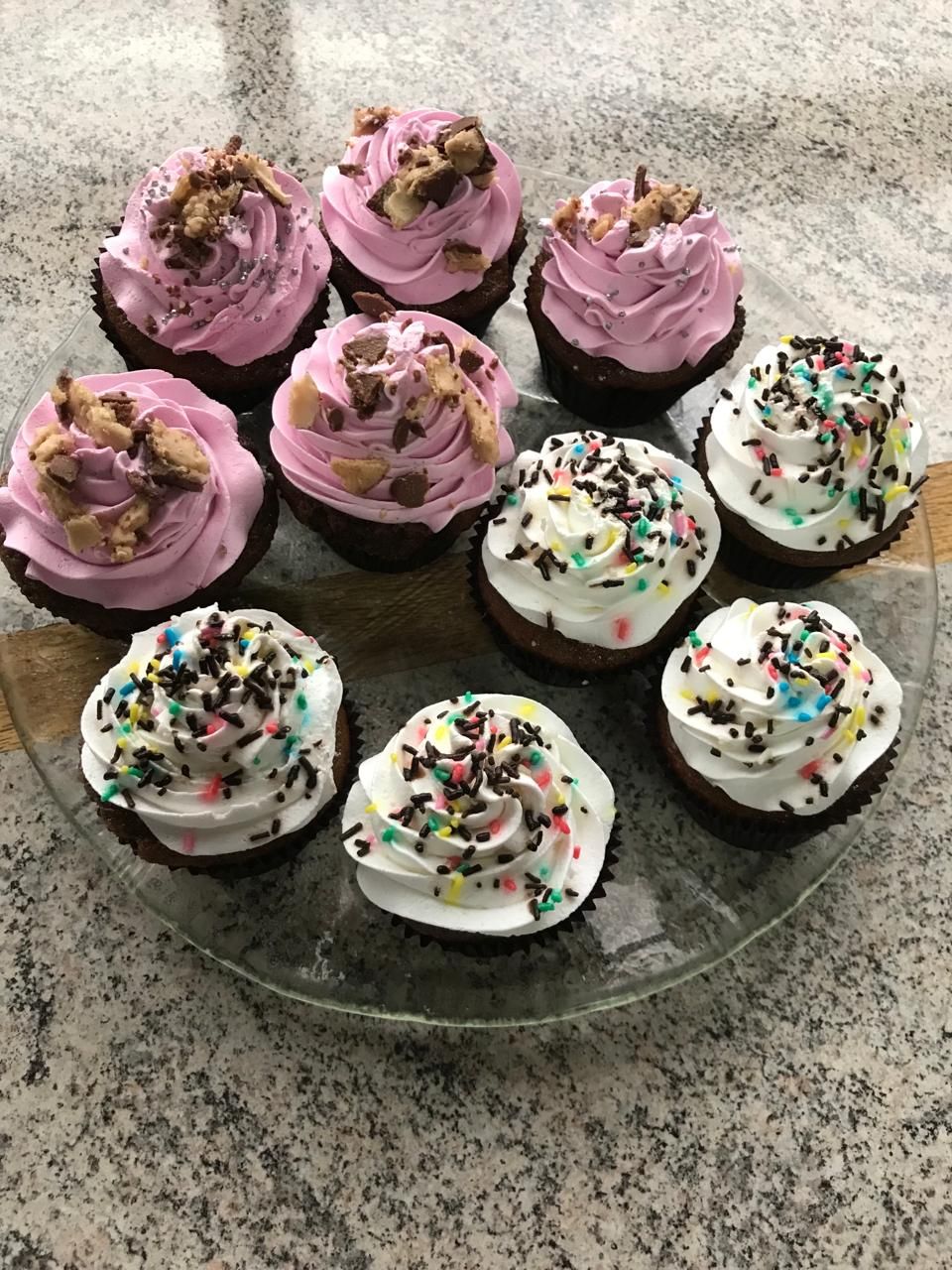 A glass plate with six cupcakes, each with different frosting and toppings.