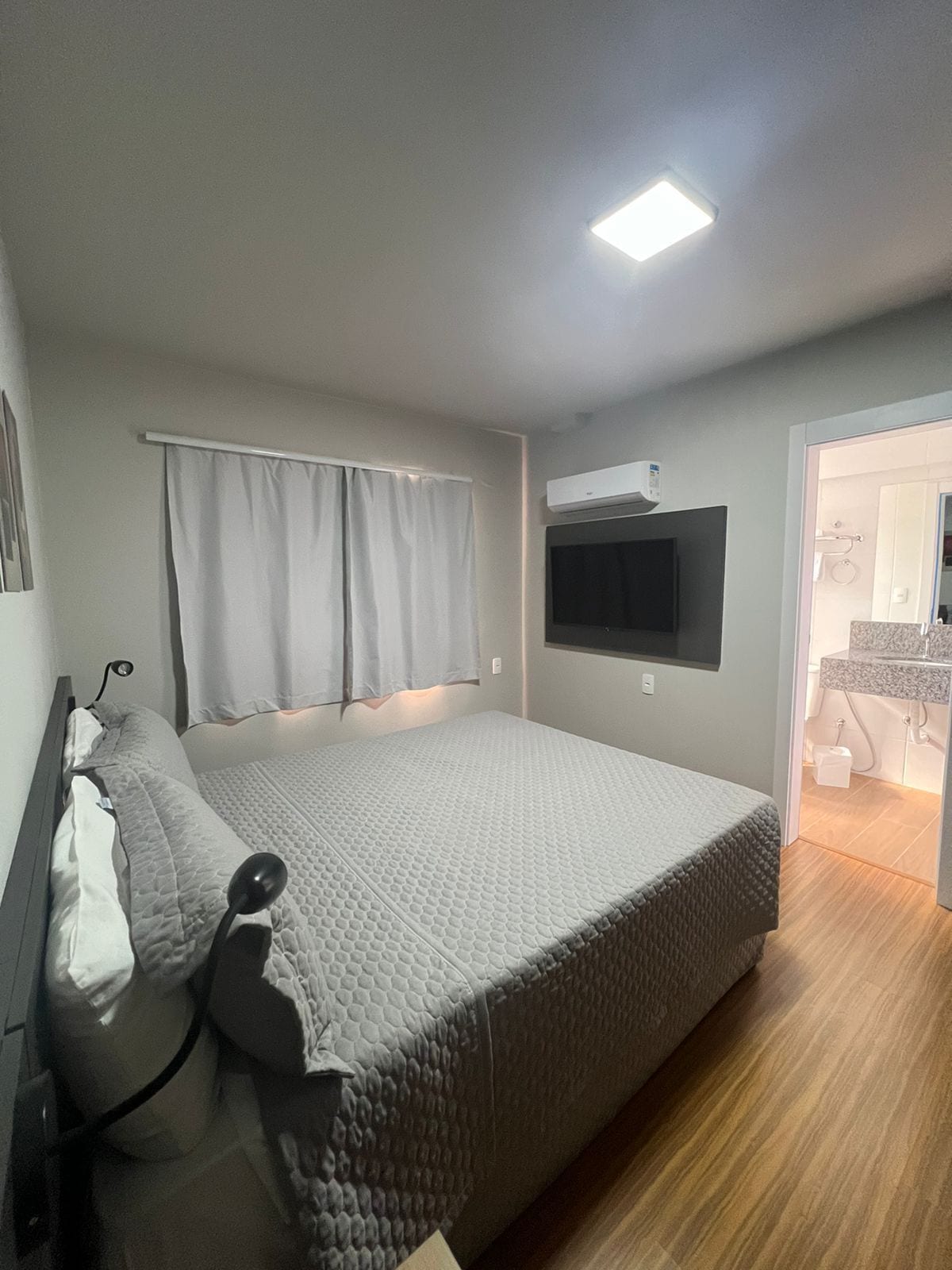 Een slaapkamer met een bed, gordijnen, een wandtelevisie en een airconditioning.
