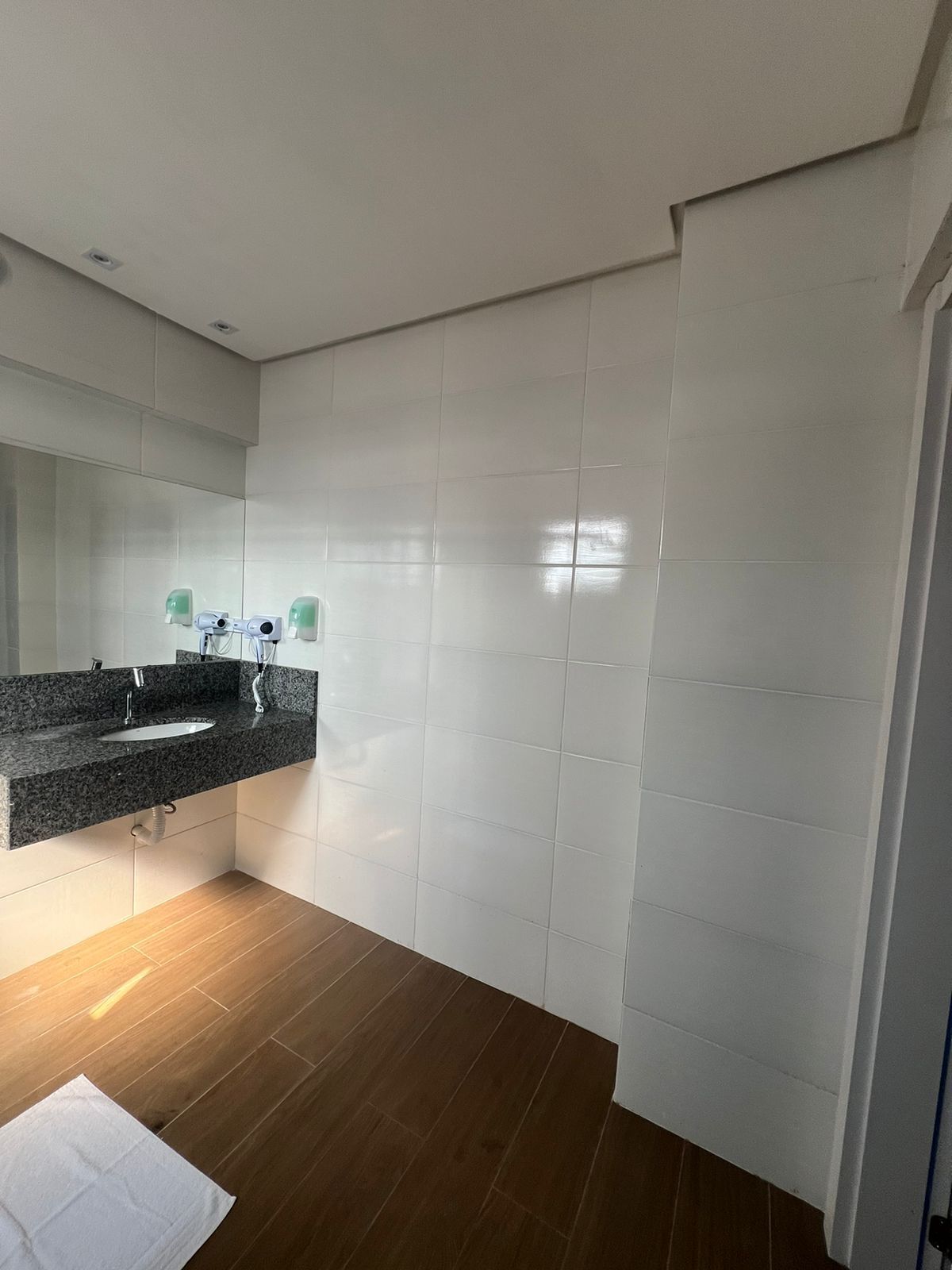 A modern bathroom with a granite countertop sink, white tiles, and a wooden floor.
