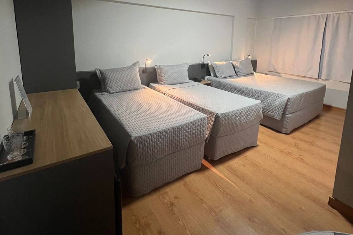 A modern hotel room with a wooden floor, a desk with a chair, two beds with pillows, and a window with curtains.