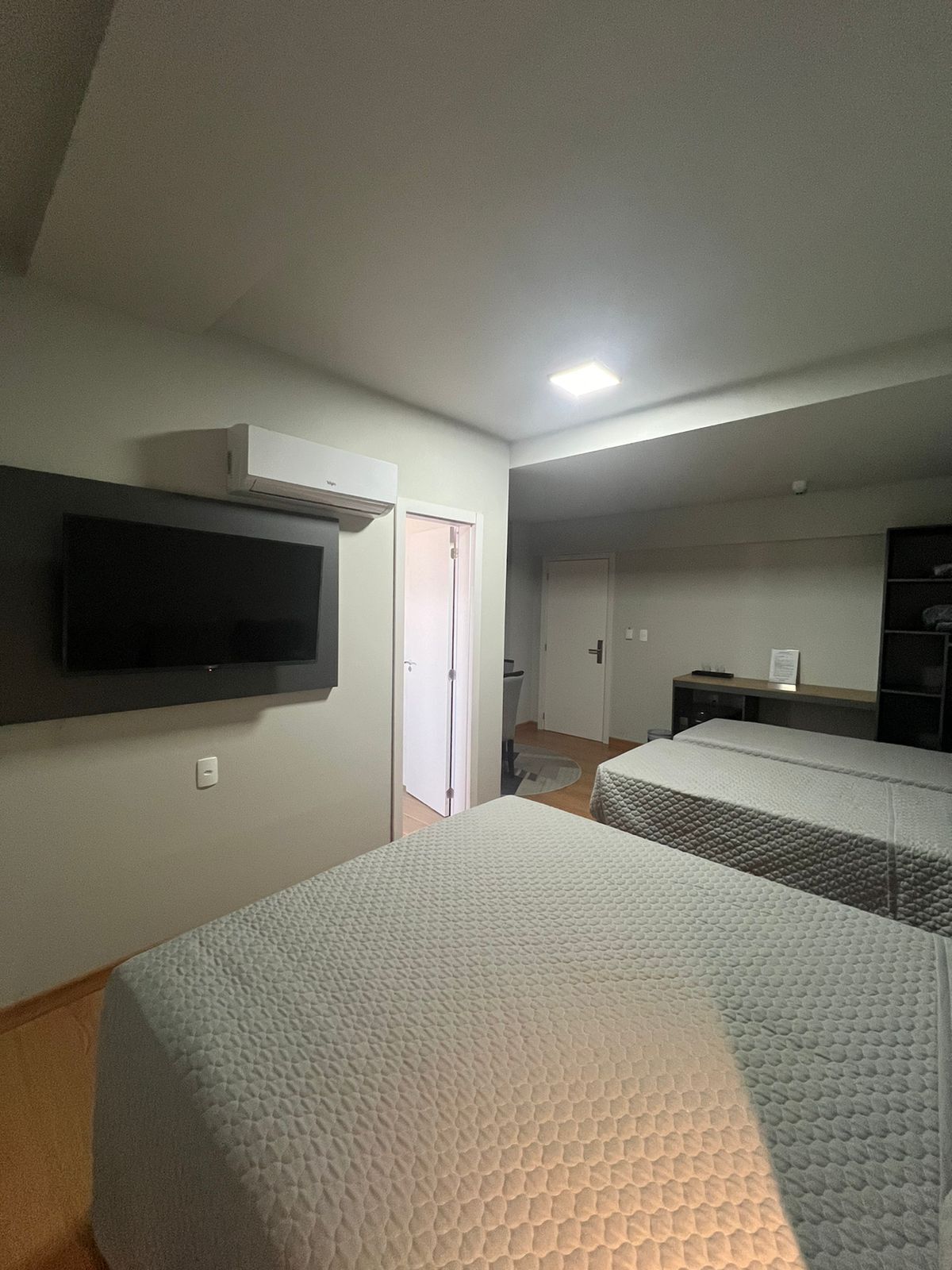 Ein Hotelzimmer mit zwei Betten, einem flachbildfernseher an der Wand, einer Klimaanlage und einem kleinen Schreibtisch mit Stuhl.