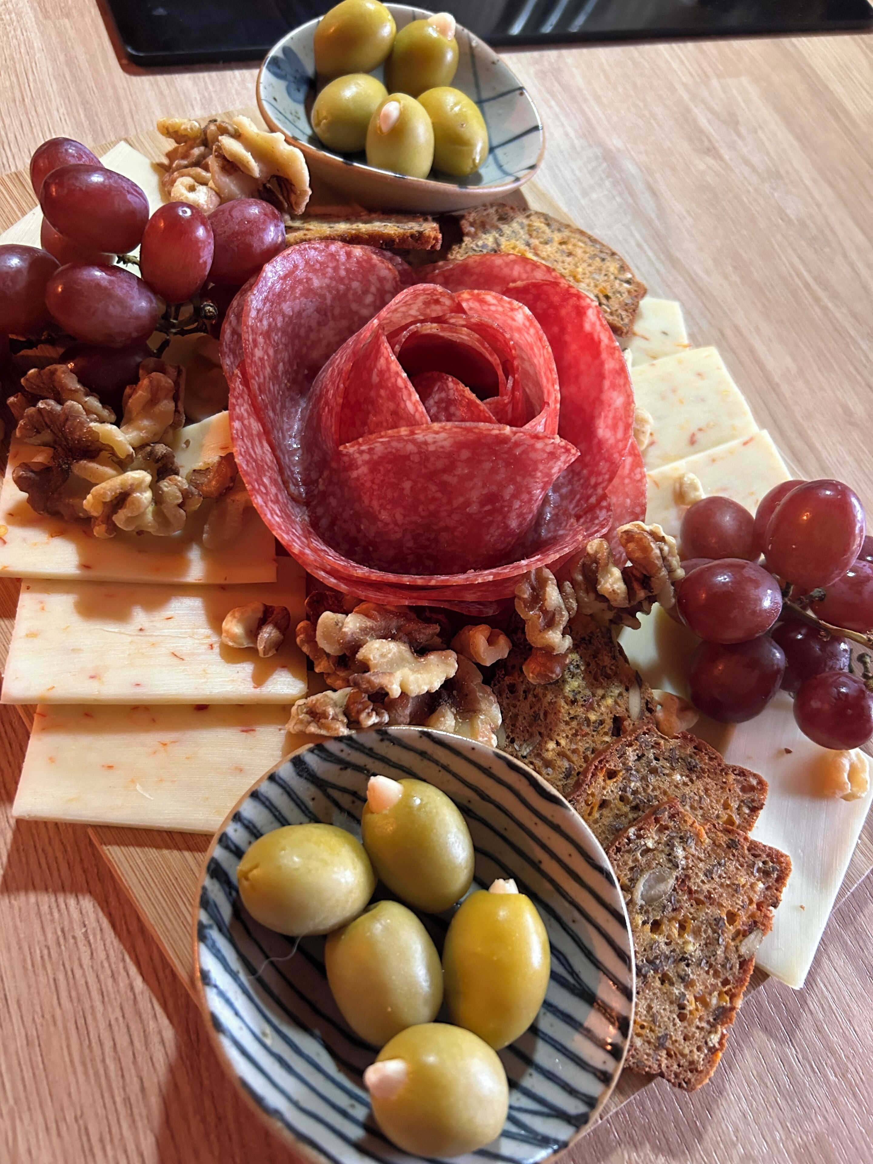 A charcuterie board with various cheeses, grapes, walnuts, and a decorative red meat rose.