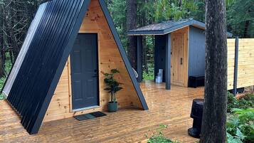 Une terrasse en bois avec une structure architecturale triangulaire, entourée d’une forêt.