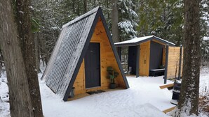 A snow-covered triangular cabin with a wooden door and a small porch area. - Private Cabin with Hot Tub, Sauna & A-Frame Bunkie – Sleeps 6 (Killaloe)