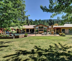 A modern house with a patio, a pool, and a large lawn.