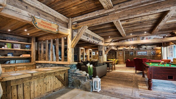 Un interior rústico de madera con mesa de billar, zona de bar y un rincón de estar acogedor.