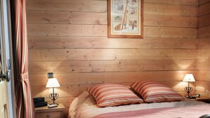 Una habitación de madera acogedora con una cama, dos lámparas de noche, un cuadro enmarcado en la pared y una silla con una manta.