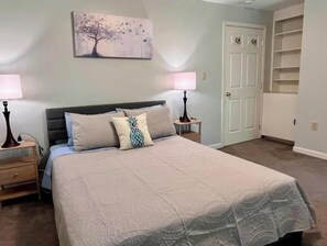 A bedroom with a bed, two bedside tables, a nightstand, a door, and a closet. - Charming 2BR w/ Garden Retreat & 2 Free Parking (Bothell)