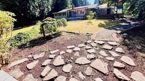 Un sendero de piedra que lleva a un edificio con porche cubierto, rodeado de árboles y un espacio verde.