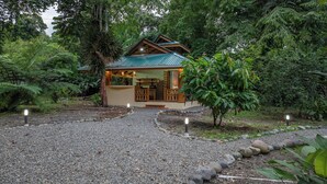 A rustic lodge with a wooden exterior, a porch, and a gravel driveway. - Tucan Chiquita Beach Casitas (Playa Chiquita)