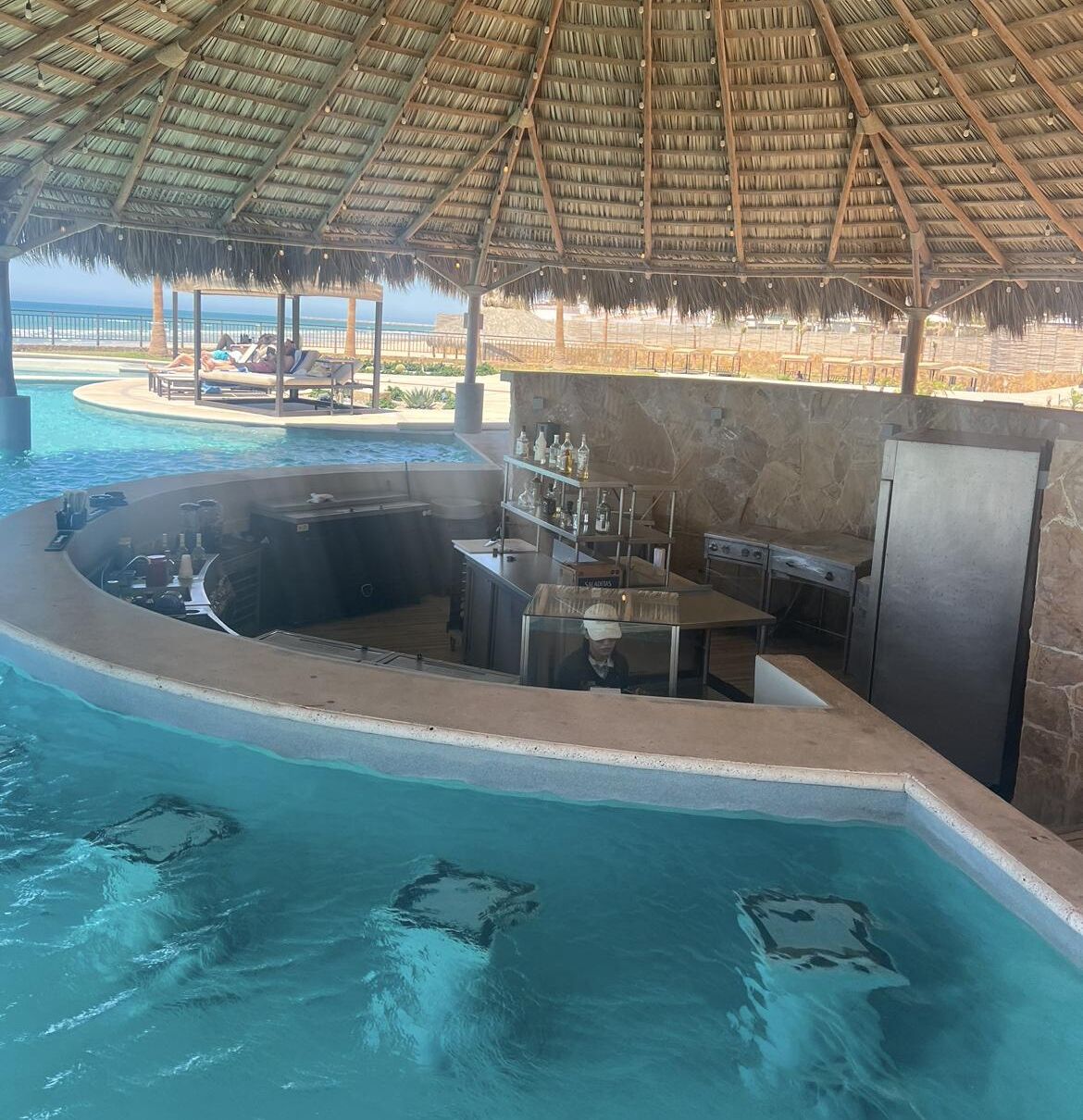 A poolside bar area with a thatched roof, a hot tub, and a bar counter.
