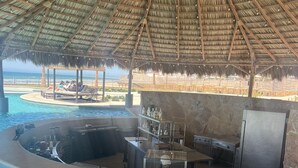 Uma área de bar junto à piscina com um telhado de palha, uma banheira de hidromassagem e um balcão de bar.