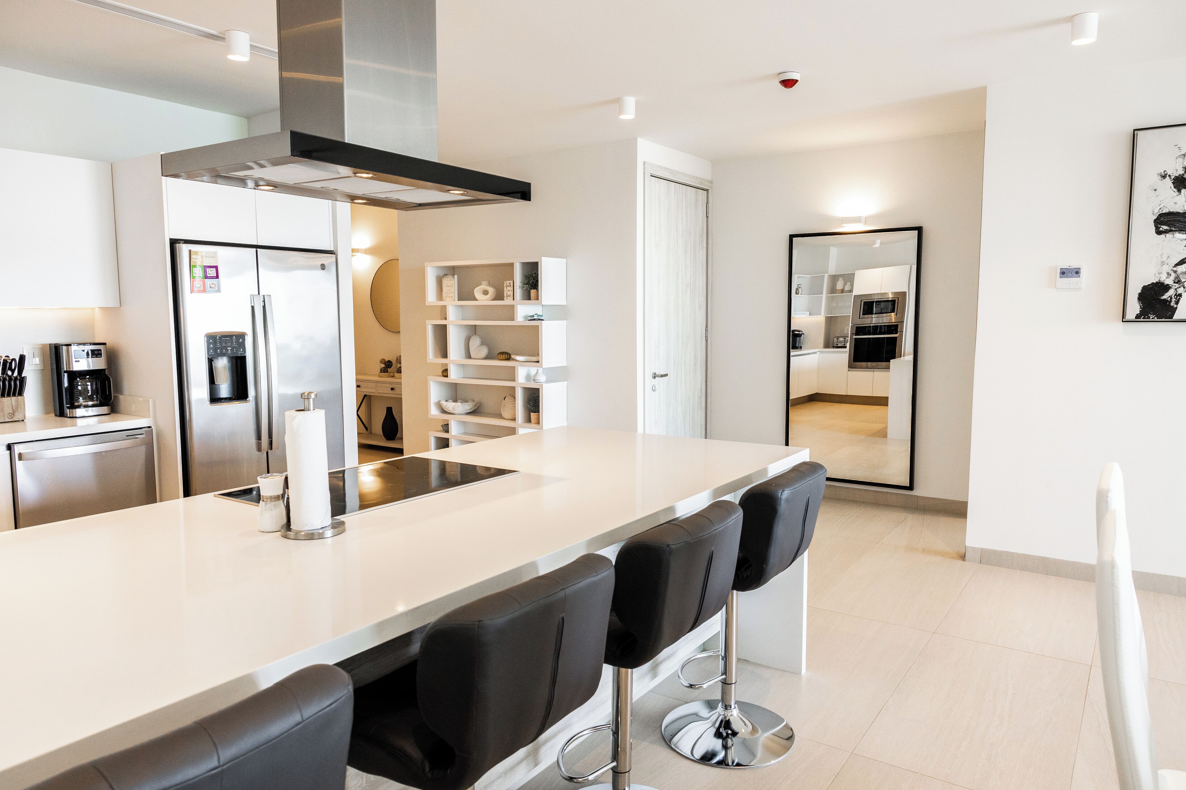 A modern kitchen with a central island, bar stools, stainless steel appliances, and a white backsplash.
