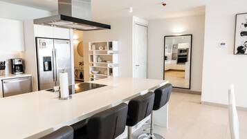 A modern kitchen with a central island, bar stools, stainless steel appliances, and a white backsplash.