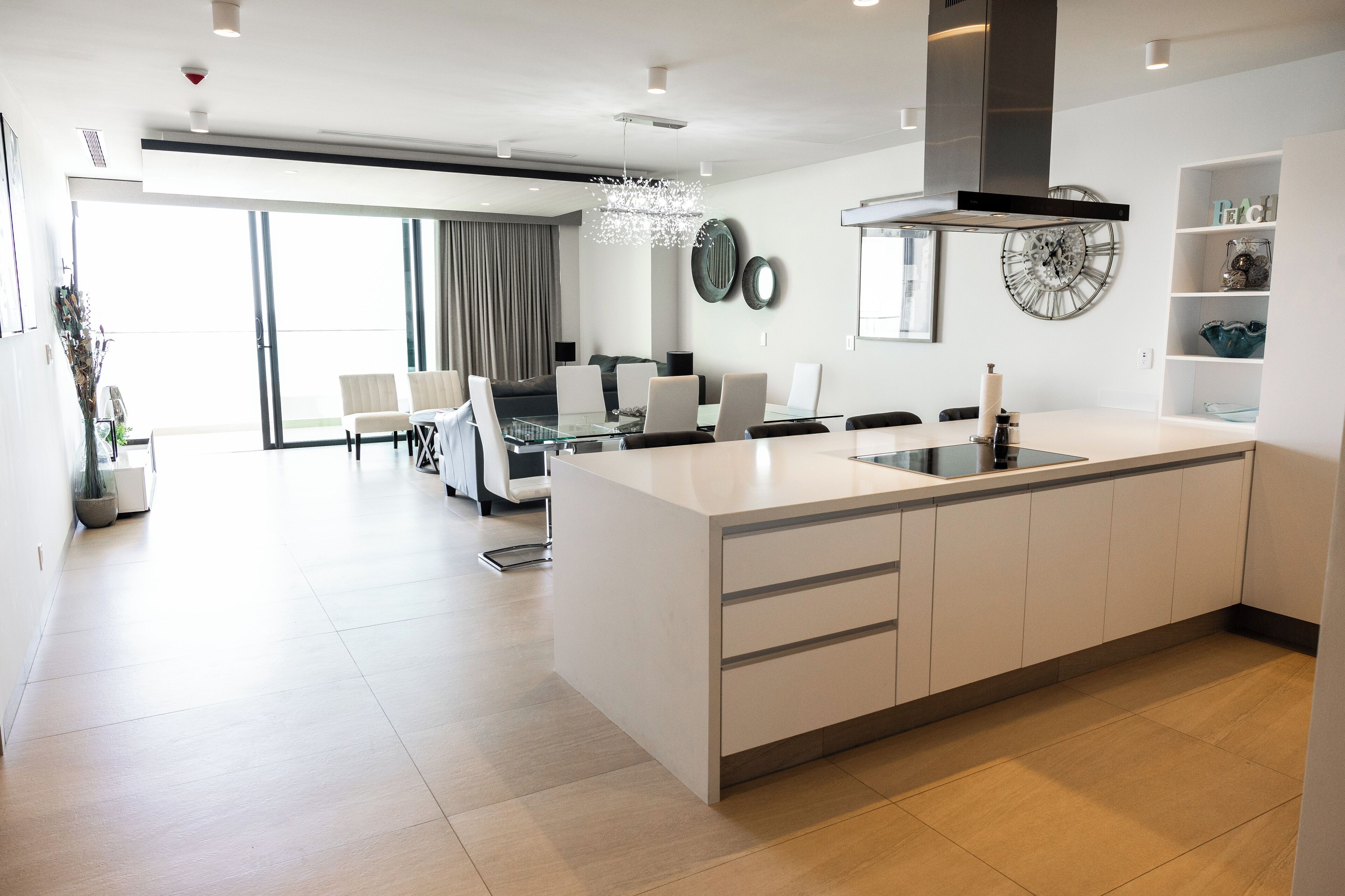 A modern kitchen with a central island, a dining area with a glass table, and a large window with curtains.