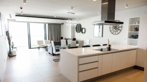 Uma cozinha moderna com uma ilha central, uma área de jantar com mesa de vidro e uma grande janela com cortinas.