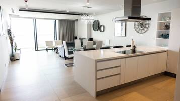 A modern kitchen with a central island, a dining area with a glass table, and a large window with curtains.