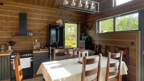 A wooden cabin interior with a kitchen, dining area, and large windows.