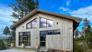 A wooden cabin with large windows, a deck, and a satellite dish.