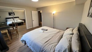 A bedroom with a bed, bedside table, lamp, and a door leading to another room. - Cozy 1 Bedroom Rental With Den Free Parking Close to University (Edmonton)