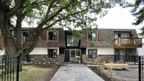 A two-story building with a stone facade, a concrete pathway, and a tree in the foreground. - Cozy 1 Bedroom Rental With Den Free Parking Close to University (Edmonton)