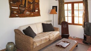 Un salon chaleureux avec un canapé en osier, une petite table en bois et un téléviseur.
