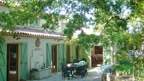 Une cour avec un sol carrelé, un espace extérieur aménagé avec des chaises et une table, et des plantes en pot.