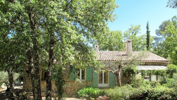 Un bâtiment rustique en pierre, doté d’un toit en tuiles, entouré d’une végétation luxuriante et d’arbres.