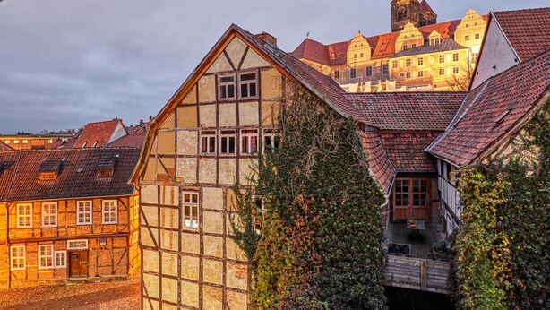 A traditional half-timbered building with a steeply pitched roof, surrounded by other historic buildings and a prominent tower in the background.