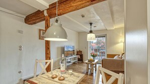 A rustic dining area with exposed wooden beams, a wooden table, and white chairs.