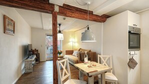 A cozy living room with a wooden table, white chairs, a sofa, and a TV.