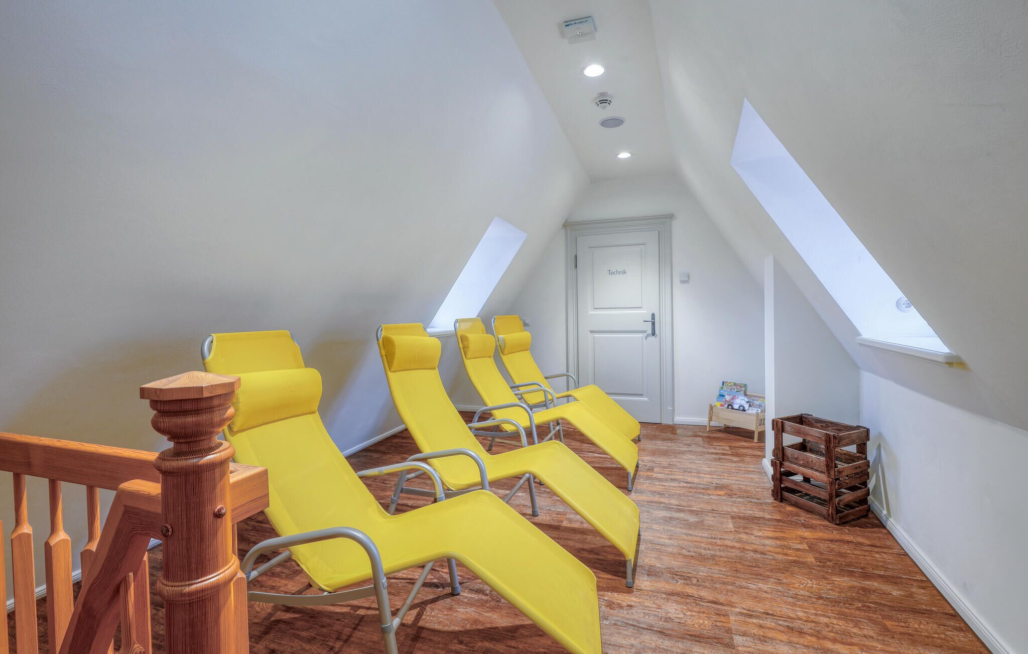 A room with yellow sun loungers, a wooden staircase, and a door labeled "Technik".