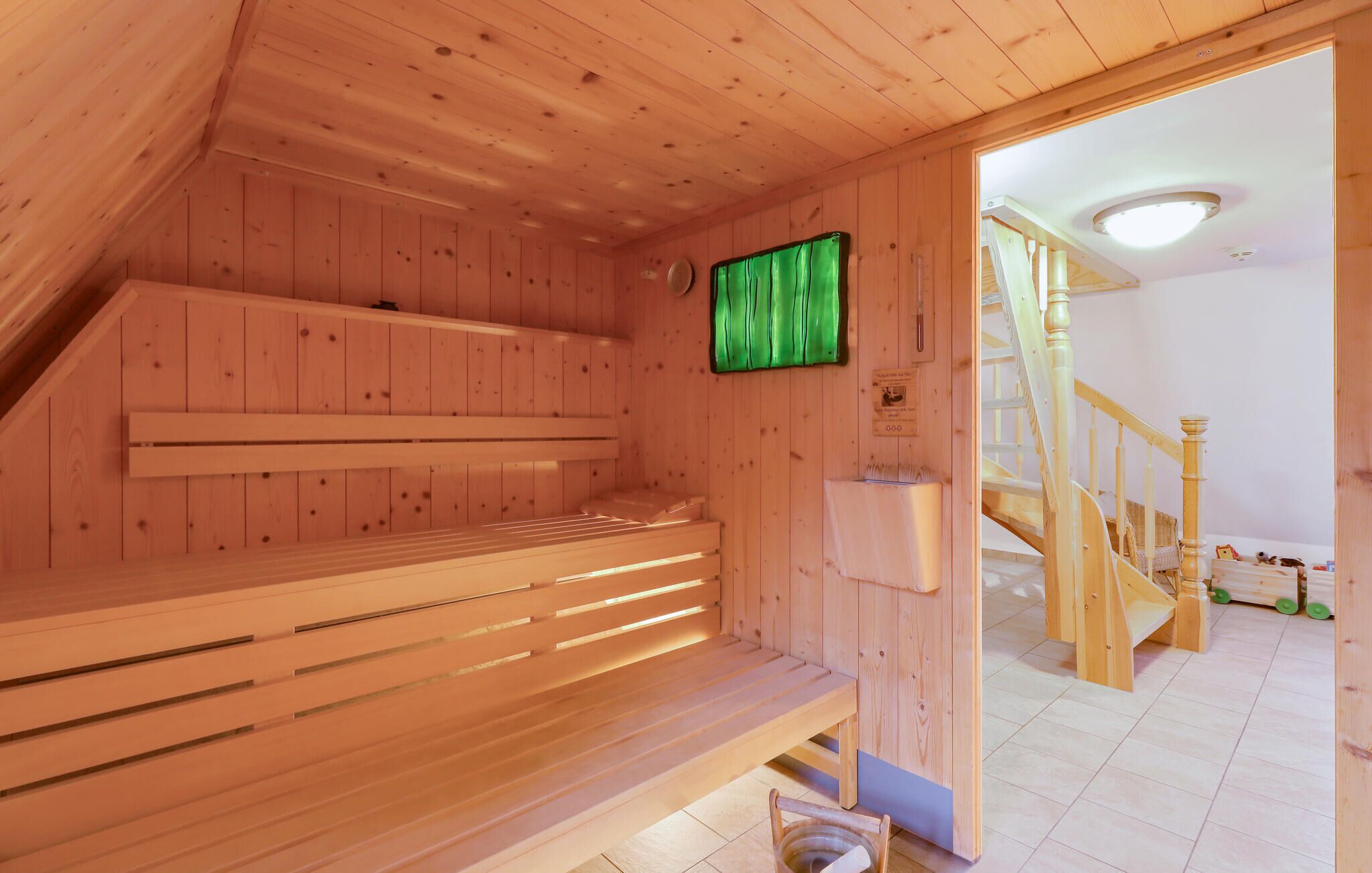 Una sauna de madera con bancos y una cortina verde, paredes de madera y una escalera que lleva a otra habitación.