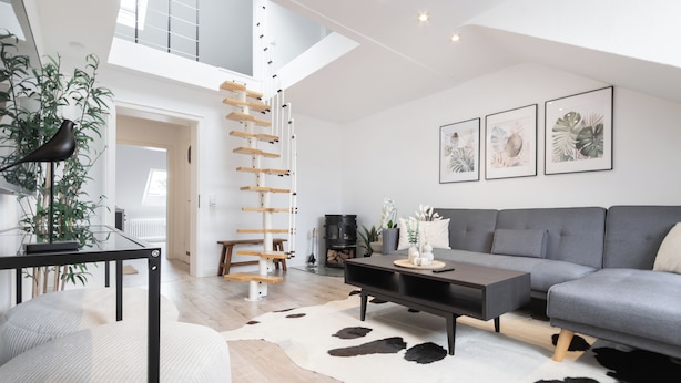 A modern living room with a grey sofa, a glass coffee table, and a black TV stand. There is a staircase leading to an upper level, and a cowhide rug on the floor. - Mc´maggies Atelier mit Insgesamt 6 Schlafplätzen (Meerbusch)